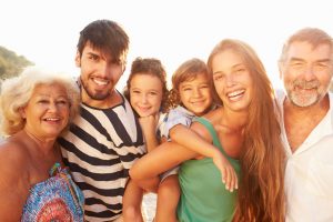 Multi Generation Family Giving Children Piggybacks On Holiday Smiling To Camera