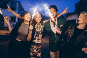 Group of friends holding sparklers out on street at night. 